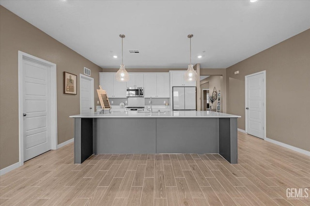 kitchen with stainless steel microwave, visible vents, white refrigerator, a large island with sink, and white cabinetry