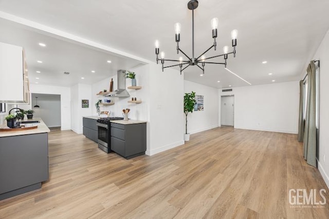 kitchen with wall chimney exhaust hood, a sink, an inviting chandelier, light countertops, and stainless steel gas range oven