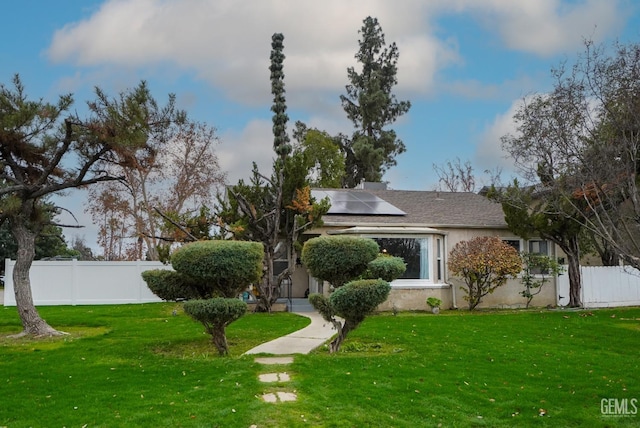 view of front of house with a front lawn, fence, roof mounted solar panels, and stucco siding