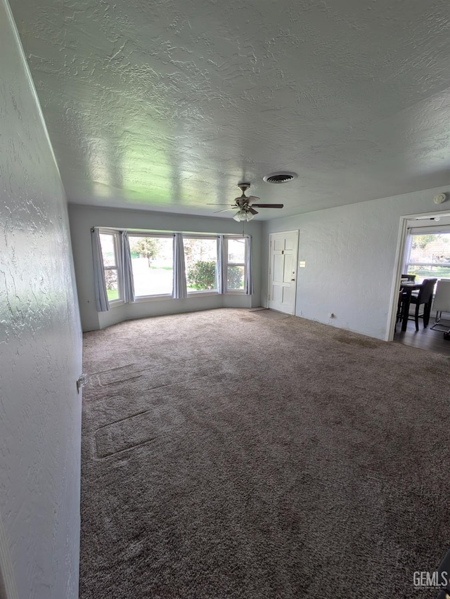 unfurnished living room with visible vents, a textured ceiling, carpet flooring, and a textured wall