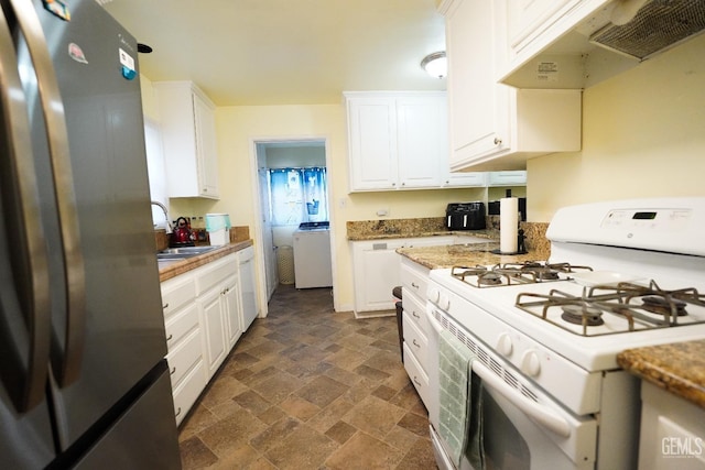 kitchen featuring under cabinet range hood, stone finish flooring, freestanding refrigerator, washer / dryer, and white gas range