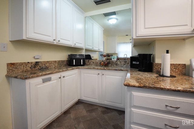 kitchen featuring stone countertops, stone finish flooring, visible vents, and white cabinetry