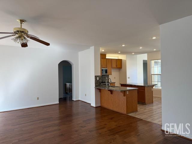 11615 Marazion Hill Ct, Bakersfield, CA 93311 - kitchen with stainless steel microwave, a peninsula, a kitchen bar, ceiling fan, and brown cabinets