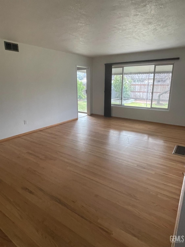 empty room with a textured ceiling and light hardwood / wood-style flooring