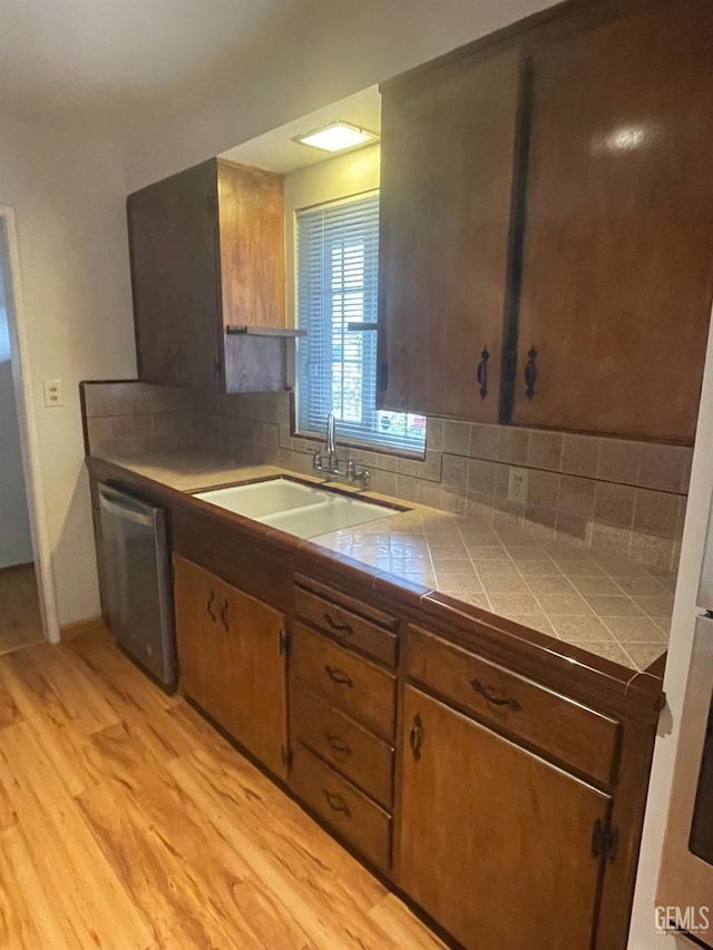 kitchen featuring dishwasher, tile counters, tasteful backsplash, sink, and light wood-type flooring