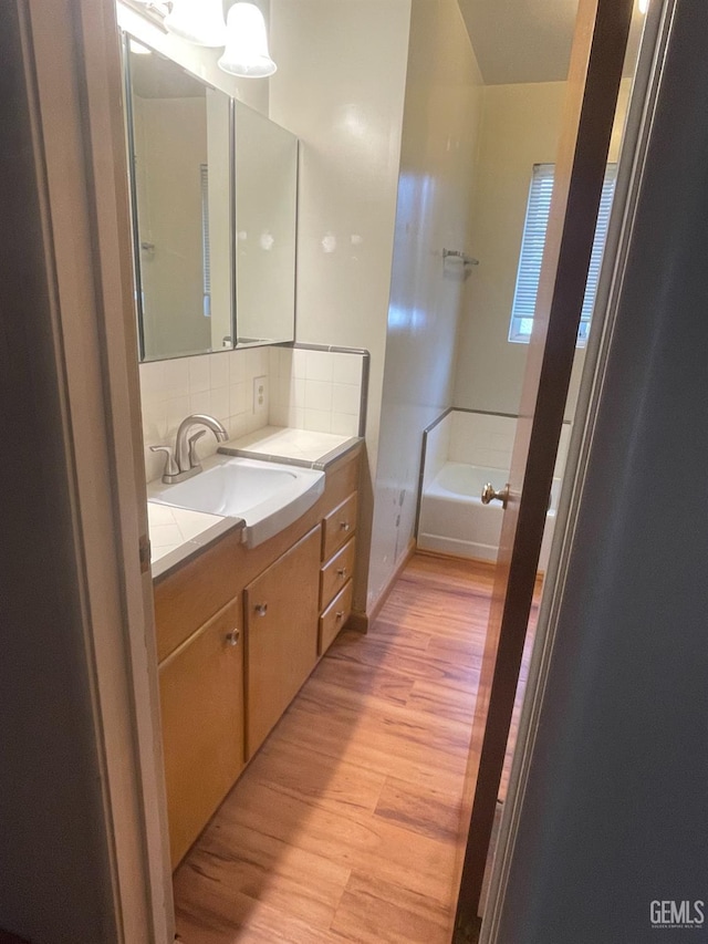 bathroom with a tub, decorative backsplash, hardwood / wood-style flooring, and vanity