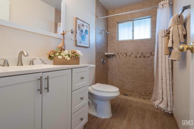 bathroom with toilet, a tile shower, wood finished floors, and vanity