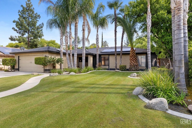 mid-century home featuring a garage, stucco siding, roof mounted solar panels, and a front lawn