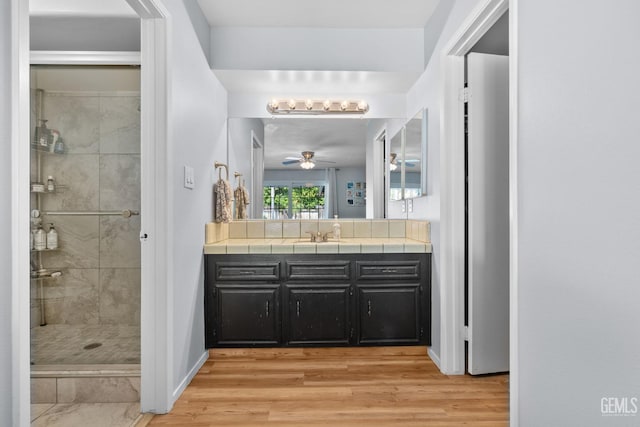 full bathroom with ceiling fan, a stall shower, wood finished floors, vanity, and baseboards