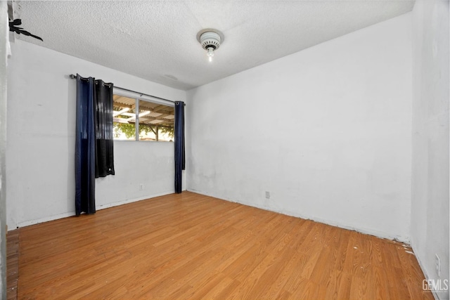 empty room with light wood-type flooring and a textured ceiling