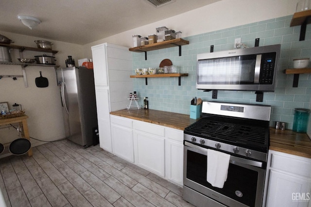 kitchen with appliances with stainless steel finishes, butcher block counters, decorative backsplash, and open shelves