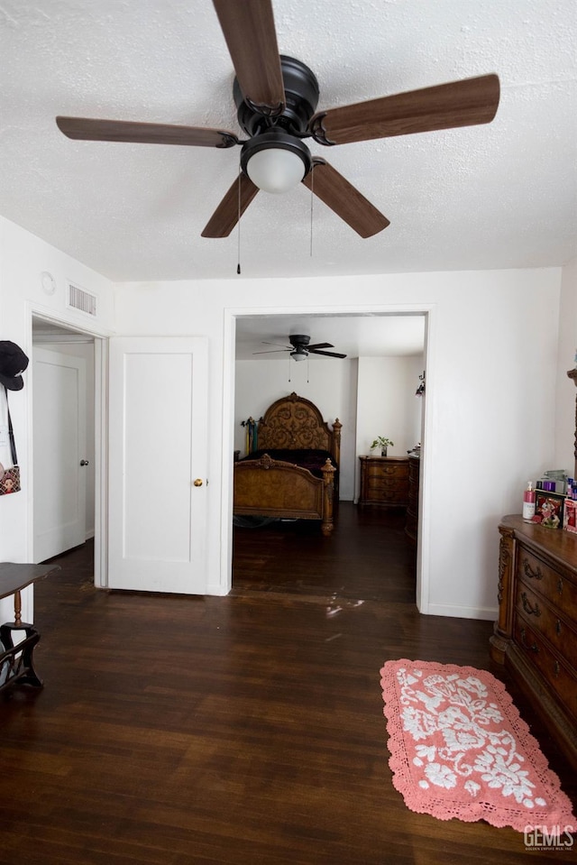 bedroom with a ceiling fan, visible vents, a textured ceiling, and wood finished floors