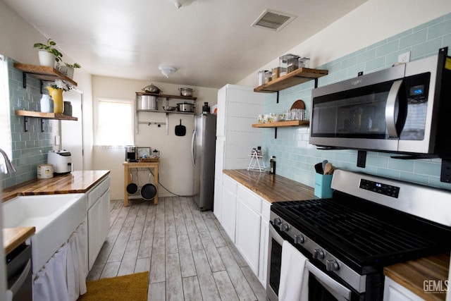 kitchen with appliances with stainless steel finishes, butcher block counters, visible vents, and open shelves