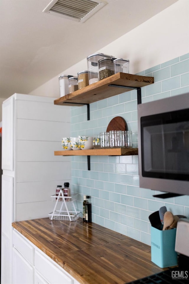 bar with visible vents, stainless steel microwave, and backsplash