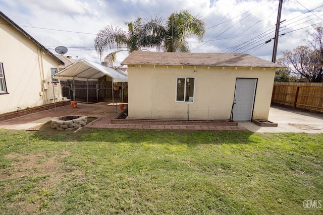 rear view of house featuring a fire pit, a lawn, a fenced backyard, an outbuilding, and stucco siding