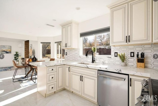 kitchen featuring a sink, dishwasher, a peninsula, and cream cabinets