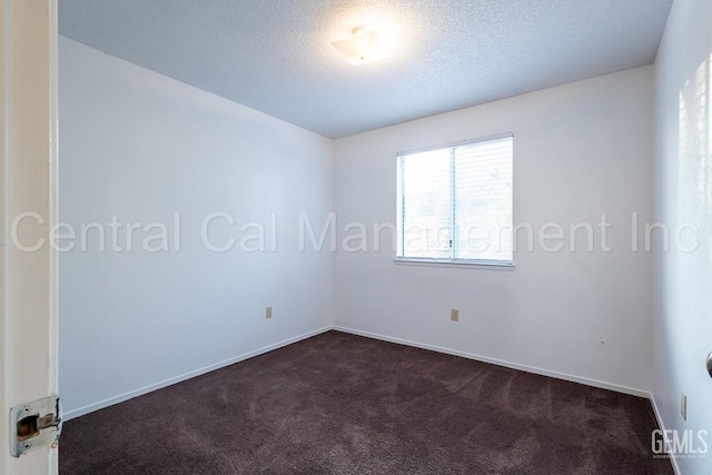 spare room featuring dark colored carpet and a textured ceiling