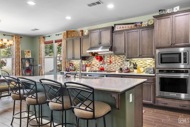 kitchen with appliances with stainless steel finishes, a breakfast bar, dark brown cabinetry, sink, and a center island with sink