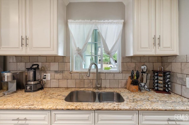 kitchen featuring white cabinets, decorative backsplash, light stone countertops, and a sink
