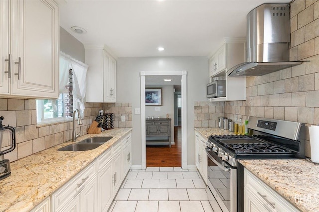 kitchen featuring stainless steel appliances, a sink, light tile patterned flooring, decorative backsplash, and wall chimney range hood