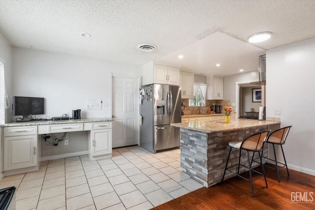 kitchen with visible vents, decorative backsplash, a textured ceiling, stainless steel refrigerator with ice dispenser, and a breakfast bar area