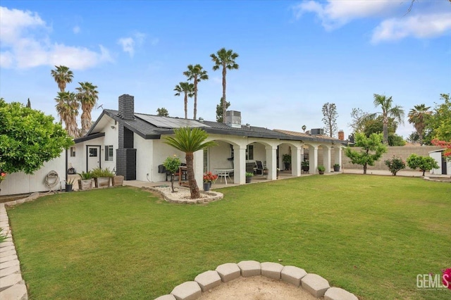 rear view of property featuring stucco siding, solar panels, a chimney, and a yard