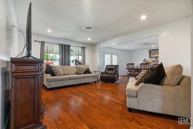living area with wood finished floors, visible vents, a textured ceiling, and recessed lighting