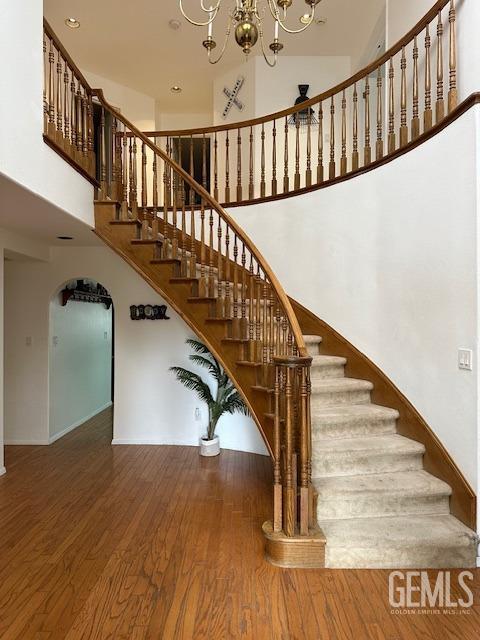 stairs featuring a chandelier, wood-type flooring, and a high ceiling