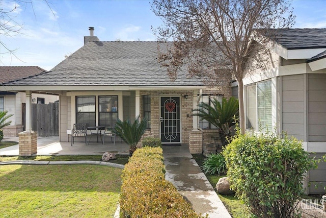 view of front of home with a shingled roof, a chimney, a front lawn, a porch, and brick siding