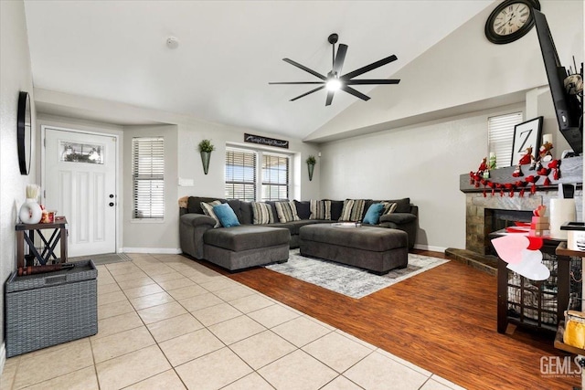 living room featuring a fireplace, light tile patterned floors, ceiling fan, vaulted ceiling, and baseboards