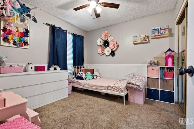 carpeted bedroom featuring a ceiling fan, a textured ceiling, and wainscoting