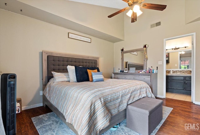 bedroom featuring baseboards, visible vents, ensuite bath, dark wood-style flooring, and a high ceiling