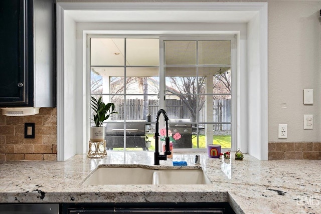 kitchen with light stone counters, tasteful backsplash, a sink, and dark cabinetry