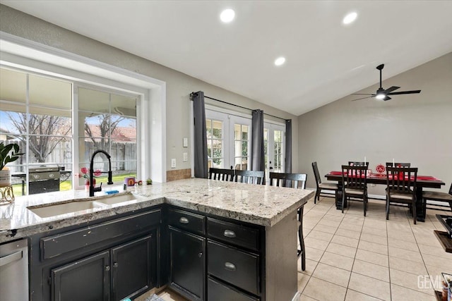 kitchen featuring light tile patterned floors, light stone counters, dark cabinetry, a kitchen bar, and a sink