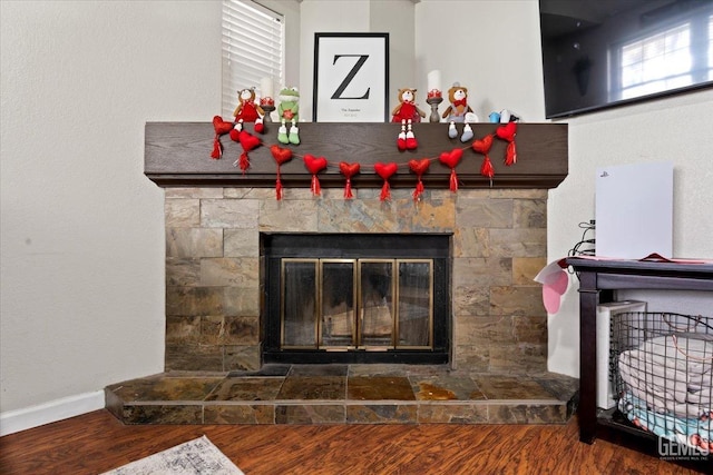 interior details with baseboards, wood finished floors, and a stone fireplace