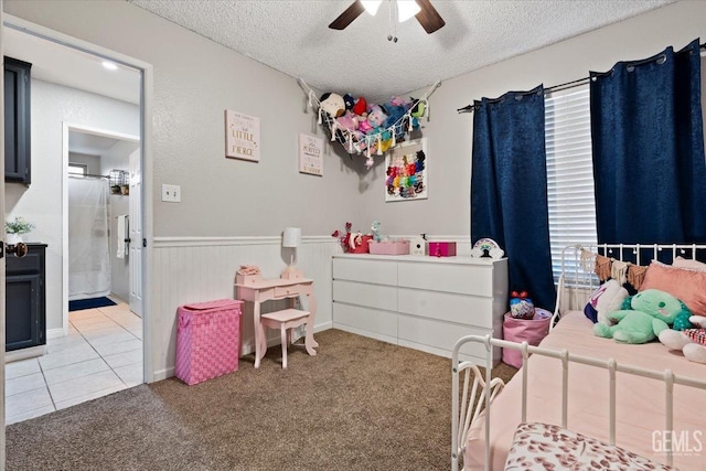 bedroom with a textured ceiling, a wainscoted wall, light carpet, and a ceiling fan