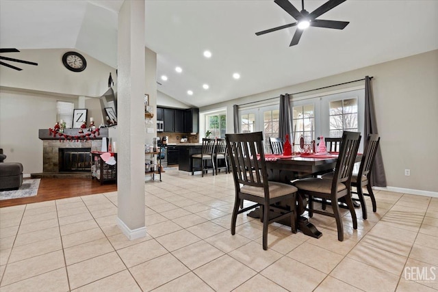 dining area featuring light tile patterned floors, a fireplace with raised hearth, french doors, and ceiling fan