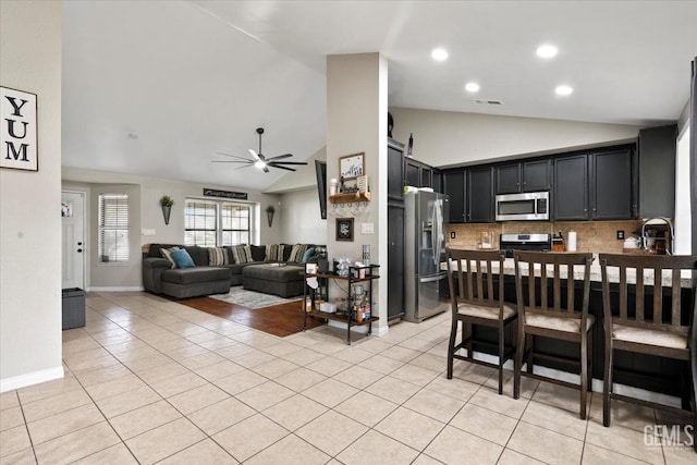 kitchen featuring a breakfast bar area, light tile patterned floors, stainless steel appliances, open floor plan, and dark cabinetry