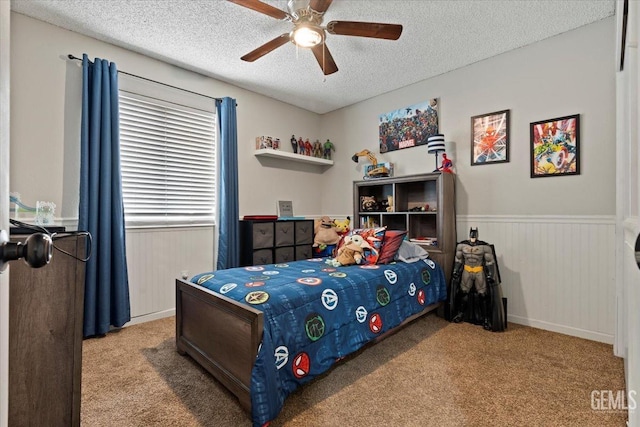 carpeted bedroom featuring a wainscoted wall, a ceiling fan, and a textured ceiling