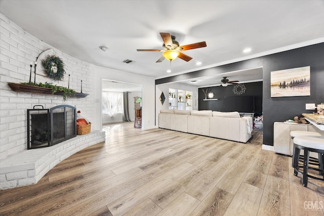 living room featuring crown molding, ceiling fan, a fireplace, and light hardwood / wood-style flooring