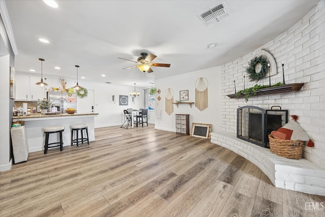 living room with a brick fireplace, ceiling fan with notable chandelier, and light hardwood / wood-style flooring