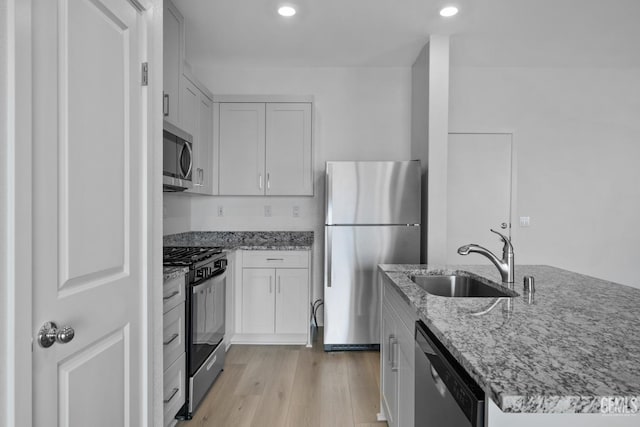 kitchen featuring sink, light hardwood / wood-style flooring, appliances with stainless steel finishes, white cabinetry, and light stone countertops