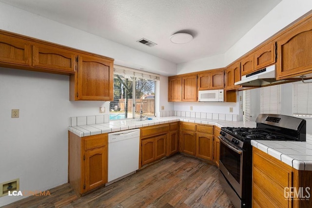 kitchen with white appliances, brown cabinets, tile counters, and under cabinet range hood