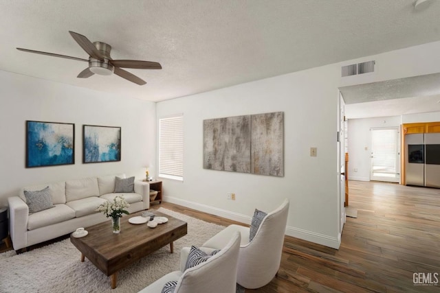 living area with a textured ceiling, dark wood-type flooring, a ceiling fan, visible vents, and baseboards