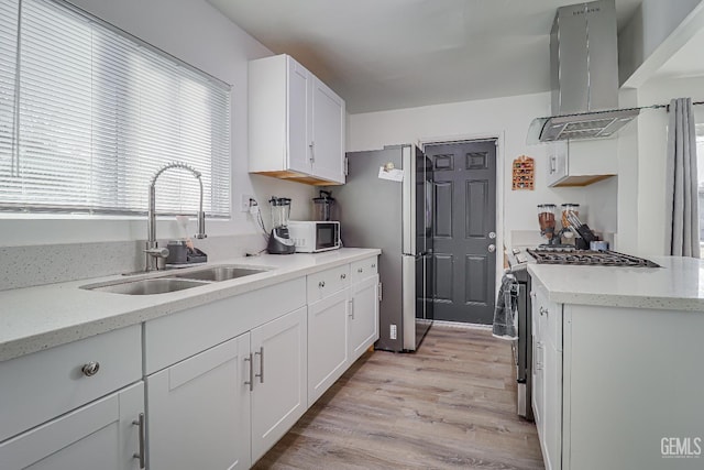 kitchen with white cabinetry, sink, island exhaust hood, light hardwood / wood-style floors, and stainless steel appliances