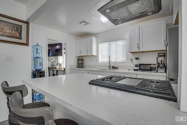 kitchen with a breakfast bar, range hood, sink, white cabinets, and stainless steel gas cooktop