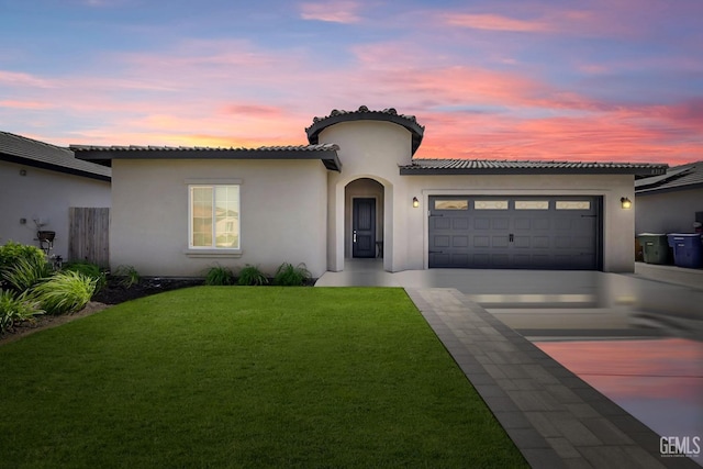 mediterranean / spanish home featuring stucco siding, an attached garage, driveway, and a yard