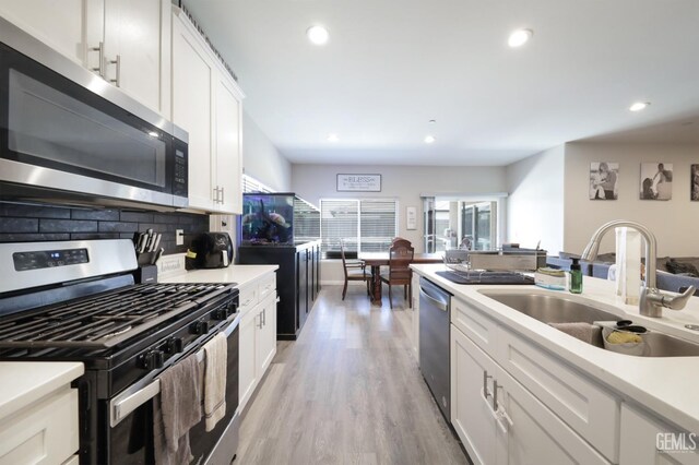 8317 Littleton St, Bakersfield, CA 93314 - kitchen with stainless steel appliances, backsplash, a sink, light wood-type flooring, and white cabinetry
