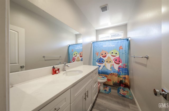 bathroom with wood finished floors, vanity, baseboards, toilet, and visible vents