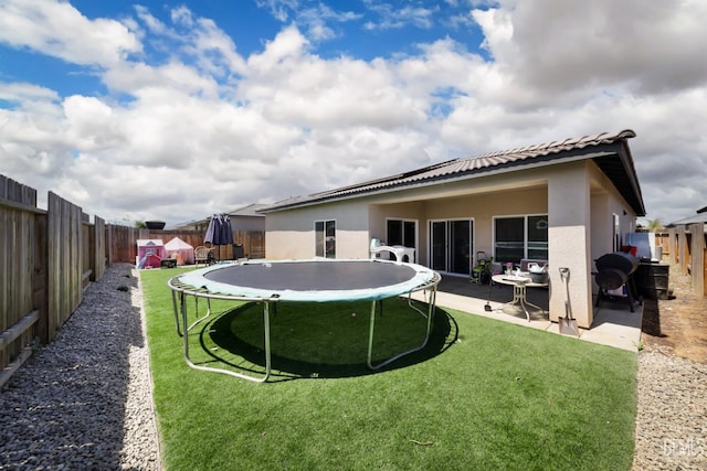 rear view of property with stucco siding, a lawn, a fenced backyard, and a trampoline